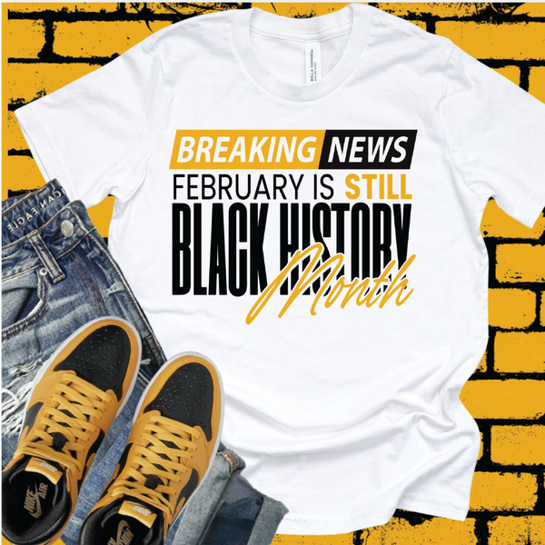 White graphic T-shirt featuring “Still Black History Month” text design, premium  printed apparel styled with denim and sneakers.