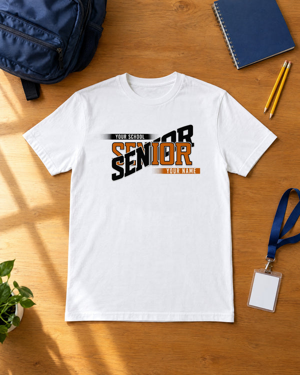 White custom Senior class year shirt in burnt orange and black laid flat on a wood desk with a school backpack, notebook, pencils and ID lanyard
