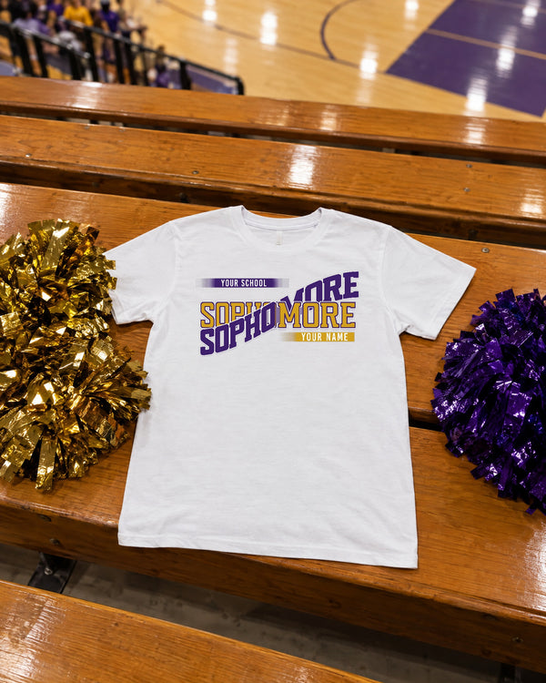 White custom Sophomore class year shirt in purple and gold laid on gym bleachers with gold and purple pom poms for a pep rally
