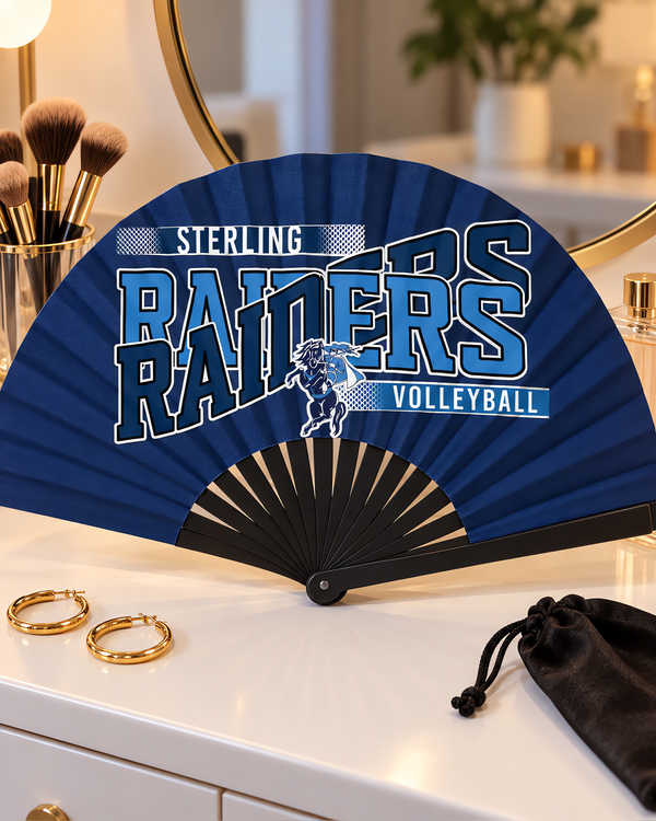 Navy game day clack fan with black ribs and a volleyball team design on a white vanity with makeup brushes and gold hoop earrings.
