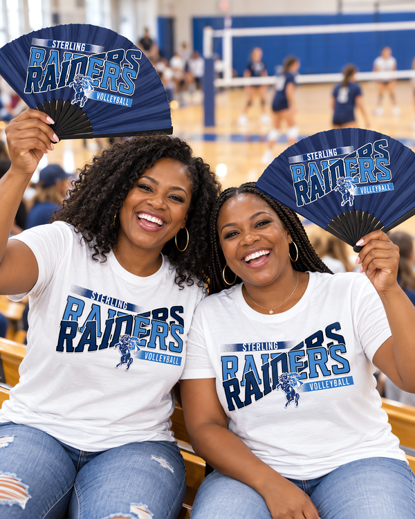 Two moms in volleyball game day shirts holding open clack fans in navy and light blue in the gym bleachers.