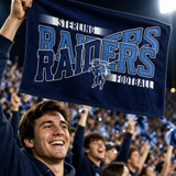 Close-up of a fan in the stands at a night game waving a navy and light blue rally towel printed with a horse and rider mascot.