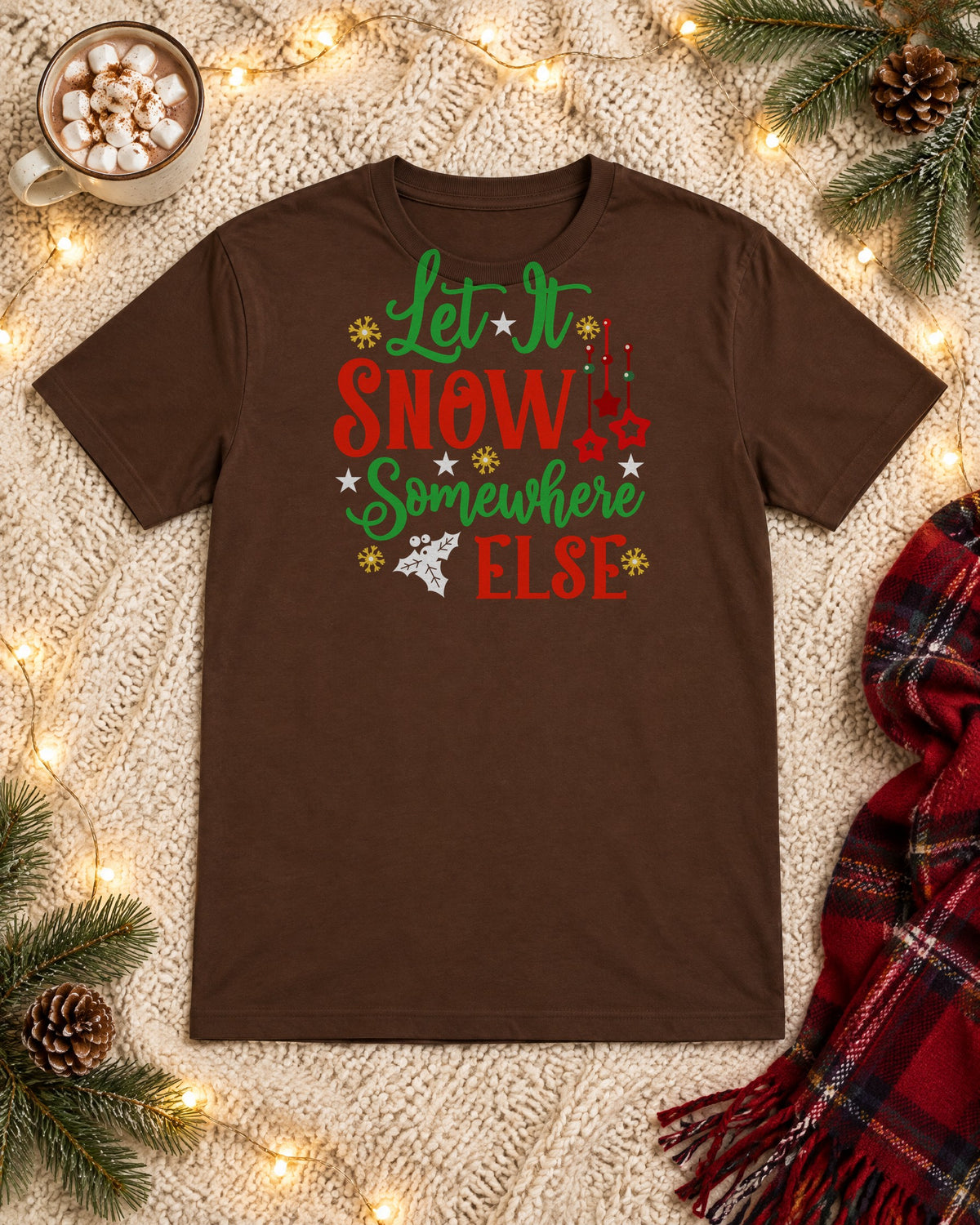 Let It Snow Somewhere Else brown graphic tee flat lay with hot cocoa, string lights and a plaid scarf