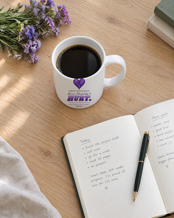 Love Shouldn't Hurt mug on a desk with a journal and purple flowers