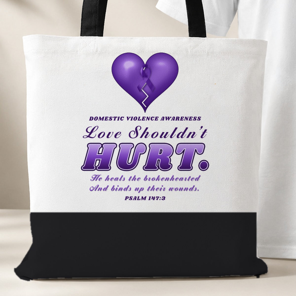 Love Shouldn't Hurt tote bag, white with a black bottom panel and black handles, purple heart and Psalm 147:3