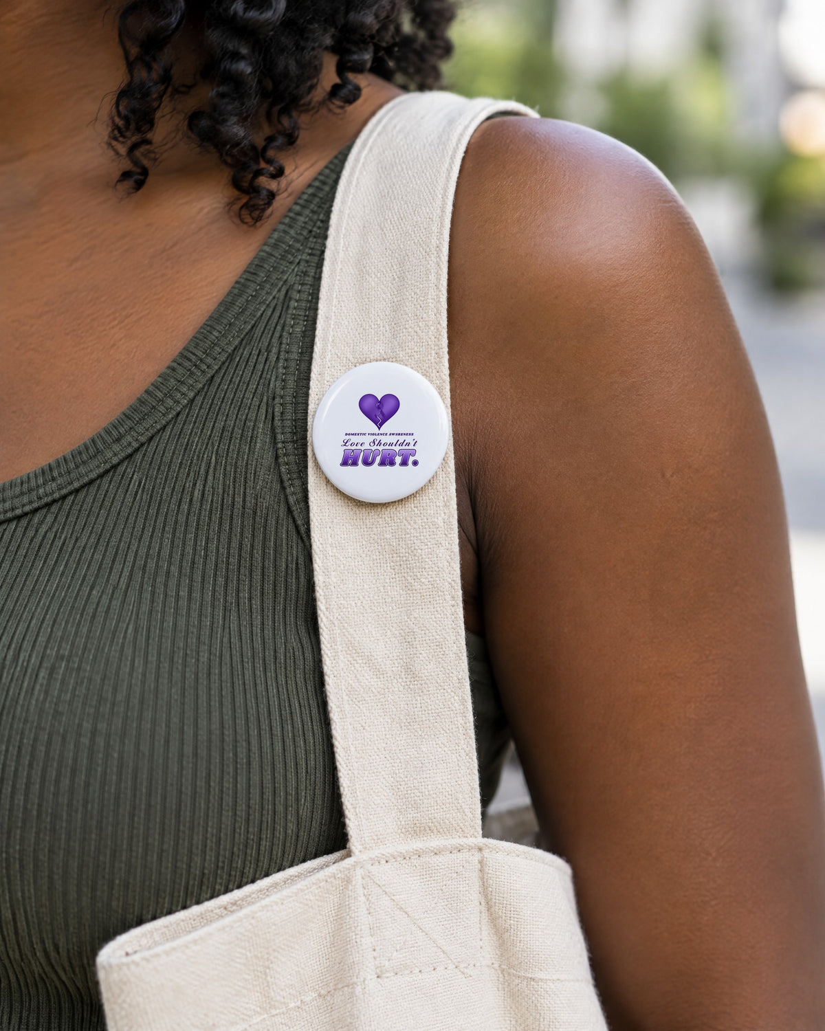 Love Shouldn't Hurt 2.5 inch sublimation button pinned on a canvas tote strap