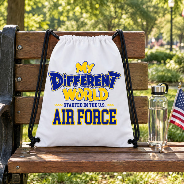 My Different World Started in the U.S. Air Force white drawstring backpack hanging on a wooden park bench, with a water bottle and a small American flag