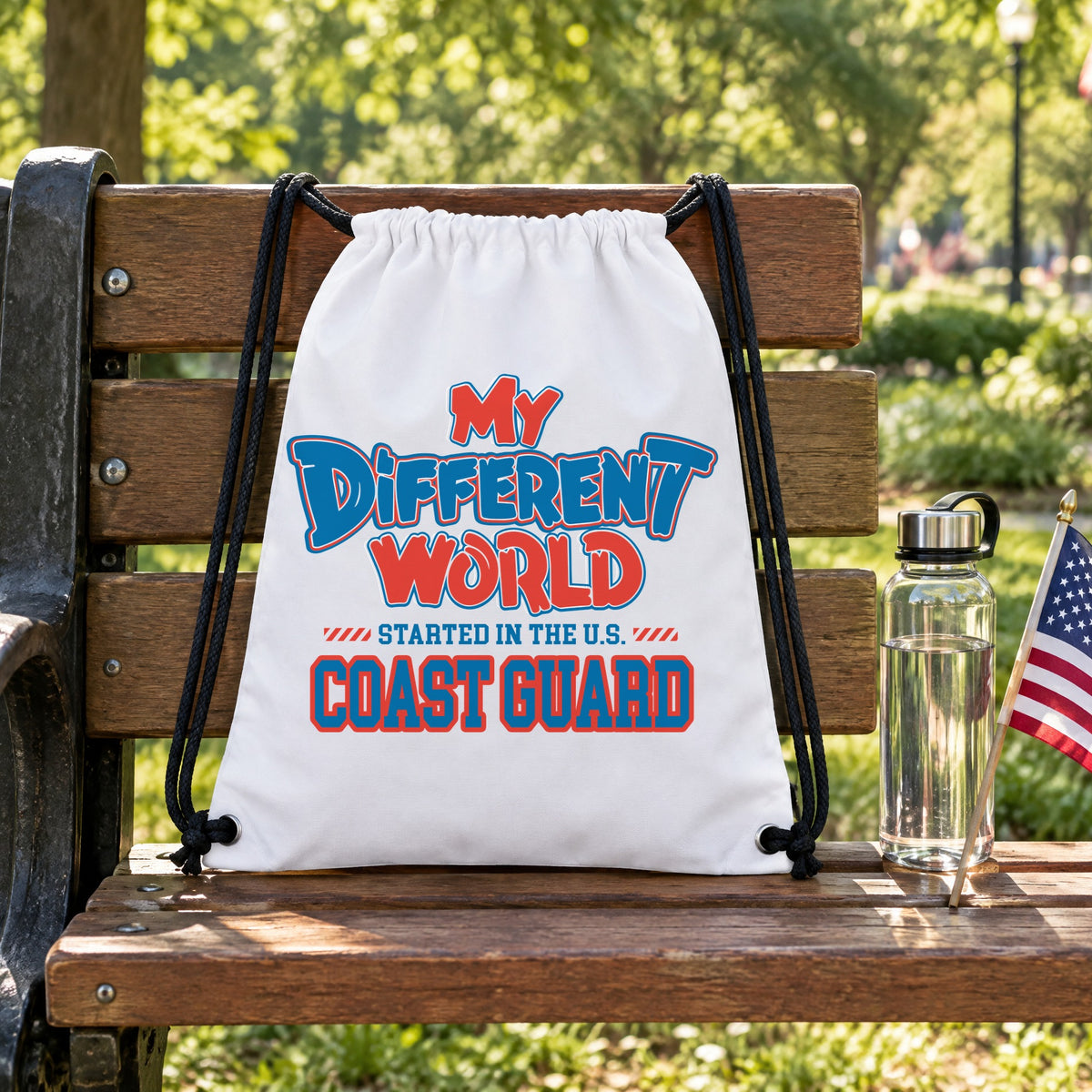 My Different World Started in the U.S. Coast Guard white drawstring backpack hanging on a wooden park bench, with a water bottle and a small American flag