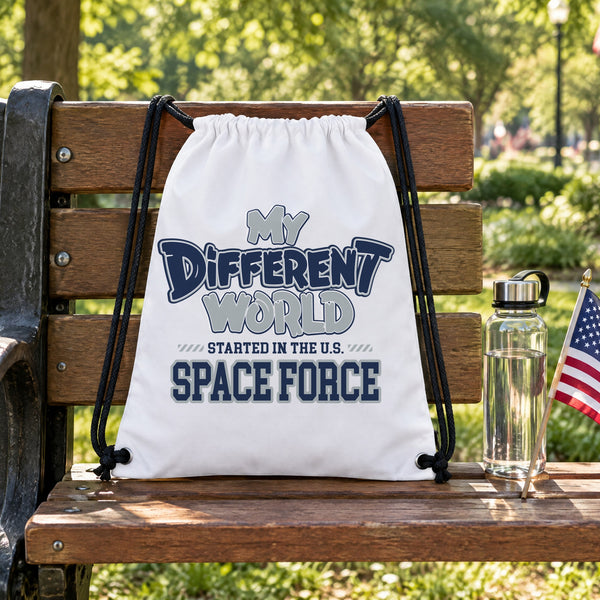 My Different World Started in the U.S. Space Force white drawstring backpack hanging on a wooden park bench, with a water bottle and a small American flag